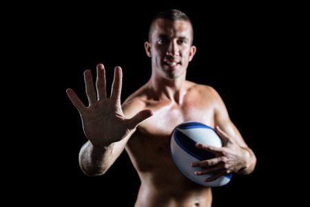 Portrait of confident shirtless sports player showing hand while holding ball against black backgroundの写真素材