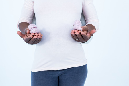 Midsection of man and woman holding baby shoes while standing against white backgroundの写真素材
