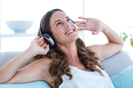 Smiling woman listening to music on sofa at homeの写真素材