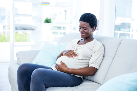 Happy pregnant woman touching her belly while relaxing at home