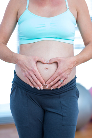 Mid section of pregnant woman making heart shape on her belly while standing in yoga classの写真素材