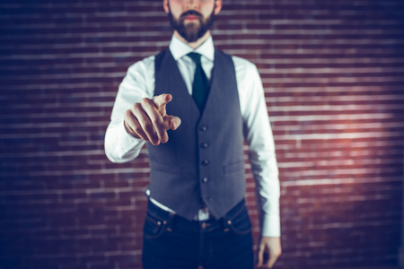 Midsection of hipster pointing finger against brick wallの写真素材
