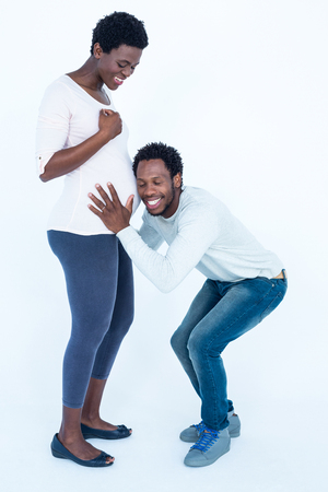 Happy husband with closed eyes listening to his pregnant wife belly against white backgroundの写真素材