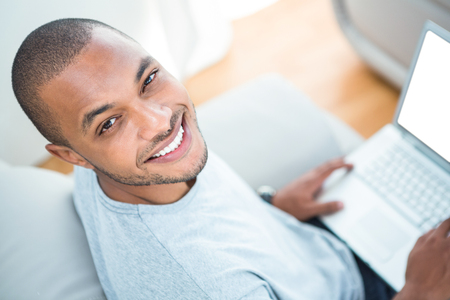 Cheerful young man with laptop on sofa at homeの写真素材