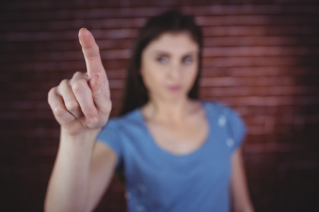 Pretty brunette pointing with finger on red brick background