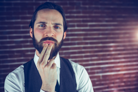 Portrait of thoughtful hipster with hand on chin against brick wallの写真素材
