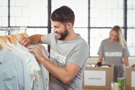 Happy man choosing clothes for donation with woman man in backgroundの写真素材