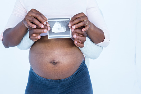 Mid section of couple holding ultrasound scan while standing against white background