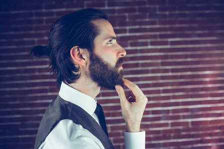 Side view thoughtful hipster with hand on chin against brick wall