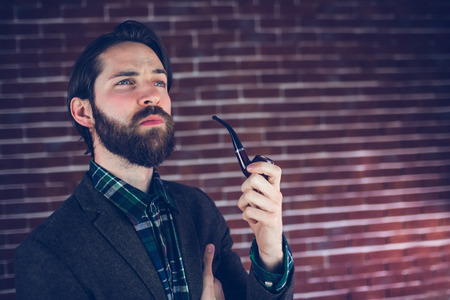 Thoughtful man smoking pipe against brick wallの写真素材