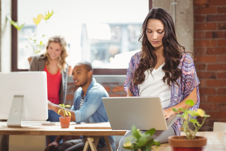 Businesswoman using laptop while colleague seen in background at creative officeの写真素材