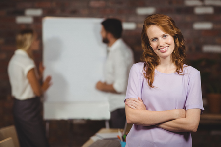 Portrait of cheerful young businesswoman with arms crossed standing in officeの写真素材