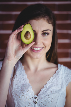 Woman showing fresh avocado on red brick background