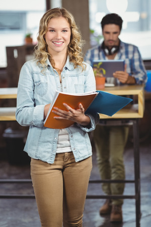 Portrait of happy businesswoman holding file while standing in creative officeの写真素材