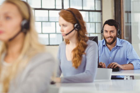 Portrait of young smiling operator with female colleagues working in officeの写真素材