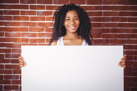 Smiling woman holding white board on red brick backgroundの写真素材