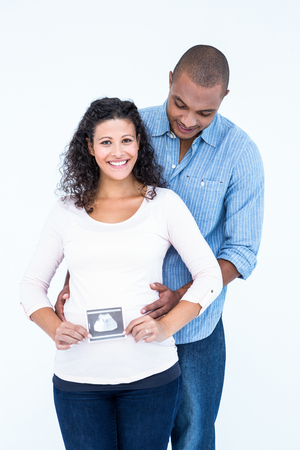 Happy pregnant woman with ultrasound scan and husband against white backgroundの写真素材