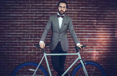 Portrait of smart confident man with bicycle against brick wallの写真素材
