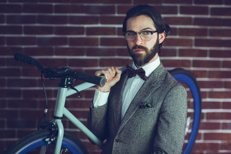 Portrait of smart confident hipster carrying bicycle against brick wallの写真素材