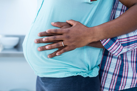 Mid section of man embracing his pregnant wife in kitchen