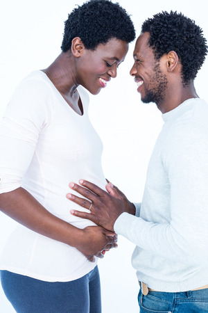 Smiling man looking at pregnant wife while touching her belly against white backgroundの写真素材