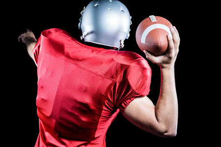 Rear view of American football player throwing ball against black backgroundの写真素材