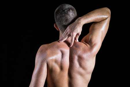 Rear view of shirtless athlete with neck pain over black backgroundの写真素材