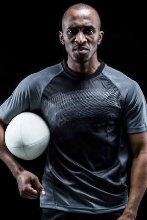 Portrait of serious athlete with rugby ball against black backgroundの写真素材