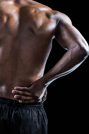 Cropped image of muscular athlete suffering through back pain against black backgroundの写真素材