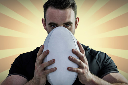 Tough rugby player holding ball against linear backgroundの写真素材