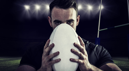 Tough rugby player holding ball against rugby stadiumの写真素材