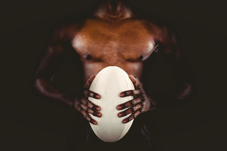 Mid section of shirtless athlete holding rugby ball over black backgroundの写真素材