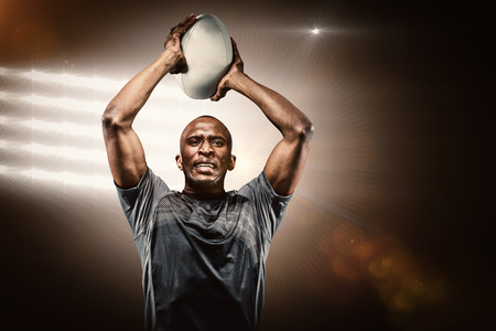 Determined sportsman throwing rugby ball against spotlightsの写真素材