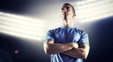 Serious rugby player looking away with arms crossed against spotlightsの写真素材
