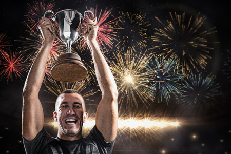 Portrait of successful rugby player holding trophy against fireworks exploding over football stadiumの写真素材