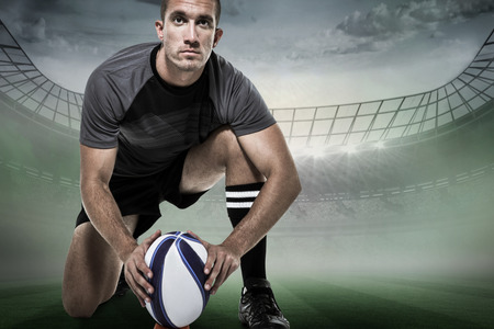 Portrait of rugby player in black jersey placing ball against rugby stadiumの写真素材