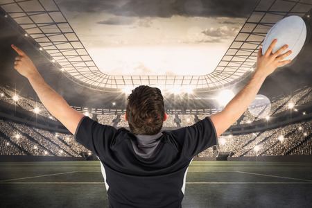 Back turned rugby player gesturing victory against large football stadium with lights