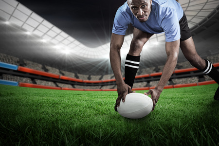 Portrait of sportsman bending and holding ball while playing rugby against rugby stadiumの写真素材