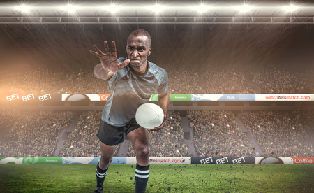 Aggressive rugby player gesturing while holding ball against rugby fans in arenaの写真素材
