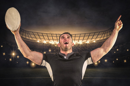 Rugby player cheering with the ball against large football stadium under night skyの写真素材