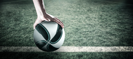 Rugby player with arm raised holding ball against rugby pitchの写真素材