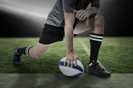 Rugby player in black jersey stretching with ball against spotlightの写真素材