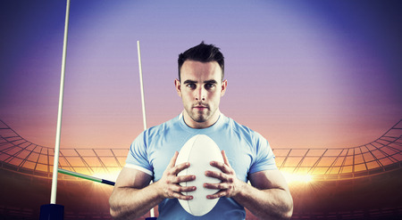 Rugby player looking at camera with ball against rugby stadiumの写真素材