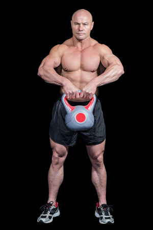 Portrait of bald man lifting kettlebell against black backgroundの写真素材