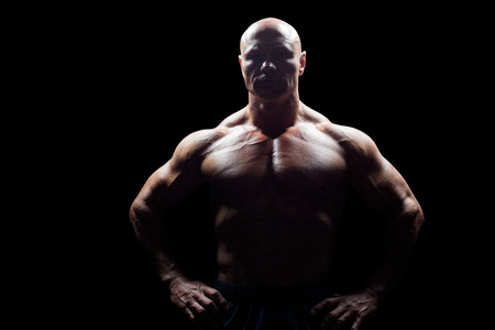 Portrait of muscular man with hands on hip against black backgroundの写真素材
