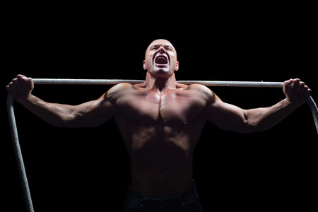 Aggressive man with arms outstretched holding rope against black backgroundの写真素材