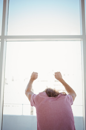 Rear view of man leaning against window glass in officeの写真素材