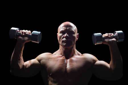 Portrait of man exercising with dumbbells against black backgroundの写真素材