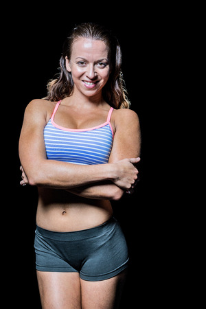 Portrait of happy athlete standing with arms crossed against black backgroundの写真素材