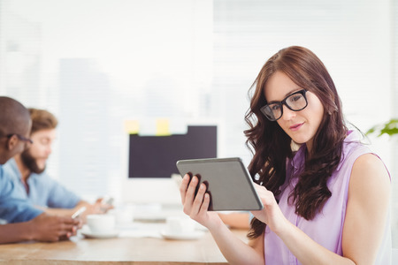 Thoughtful woman holding digital tablet at desk in officeの写真素材
